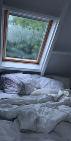 an unmade bed sitting under a window in a room with white sheets and pillows