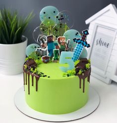 a birthday cake decorated with minecraft figures and decorations on a table next to a potted plant