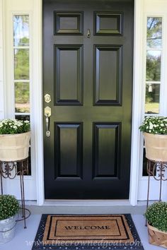 a black front door with two planters on either side and welcome mat in front