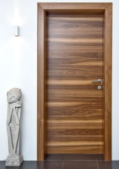 a wooden door in a white room next to a vase with a statue on the floor