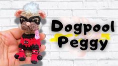 a hand holding a small crocheted toy with the words dogpool peggy on it