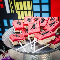 some red and white treats are on a silver platter with candy sticks in the shape of spider webs