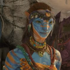 a woman with painted face and body is standing in front of a rock formation wearing jewelry