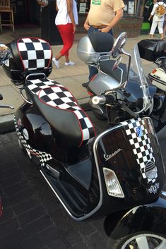 two motorcycles with checkered seats are parked on the side of the street while people walk by