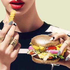 a woman is eating a large hamburger while wearing gold rings and holding a fork in her hand