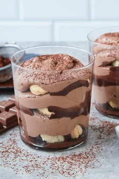 two glasses filled with chocolate dessert on top of a table