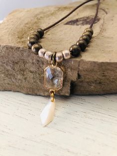 This neutral boho necklace has a rich brown genuine leather cord.   Strung on the leather are classic bronze brass beads as well as intricately handmade silver African brass beads.  It's focal point contains a luxe faceted crystal pendant accompanied by a simple, yet refined, mother of pearl bead.  This piece expresses femininity with a modern rustic style.  The cord measures 26 inches and the pendant is 1 3/4 inches in length. Bohemian Adjustable Faceted Crystal Necklaces, Modern Rustic Style, African Brass Beads, Boho Necklaces, Neutral Boho, Brass Beads, Necklace Boho, Jewelry Stand, Faceted Crystal