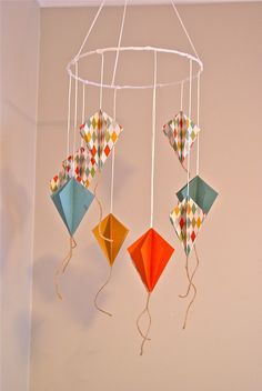 three colorful kites hanging from a white wire in the corner of a room with a pink wall