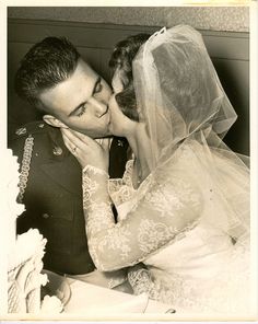 an old photo of a bride and groom kissing each other in front of a cake