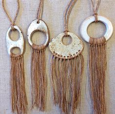 four different necklaces are hanging on the wall with tassels attached to them