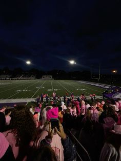 a large group of people standing on top of a football field at night with the lights on