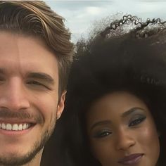 a man standing next to a woman smiling at the camera with her hair blowing in the wind