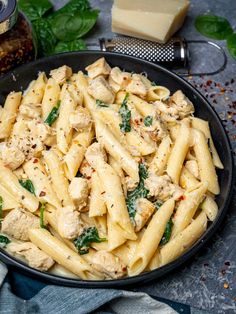 pasta with chicken, spinach and cheese in a skillet next to some parmesan cheese