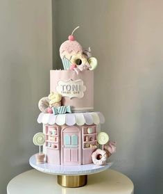 a pink and white cake with an ice cream shop on top is sitting on a table