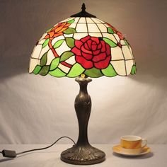 a lamp with a rose on it next to a cup and saucer in front of a white background