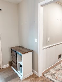 an empty room with white walls and wood flooring in the foreground, there is a small cabinet next to it