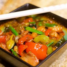 a square bowl filled with stir fry vegetables and chopsticks on top of a table