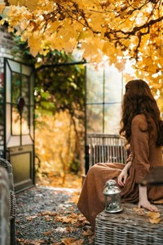 a woman sitting on a bench next to a tree with yellow leaves in the fall