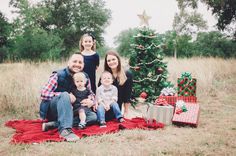 a family sitting on a blanket in front of a christmas tree