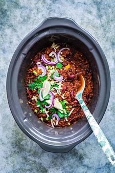 a bowl filled with chili and onions on top of a table next to a spoon