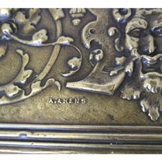 an ornately decorated silver box with writing on the front and bottom, inlaid with images of men's heads