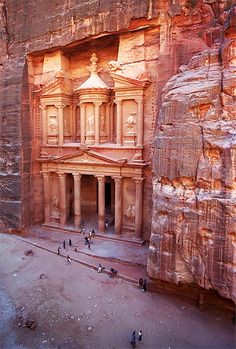 an old building in the middle of a large stone wall with people walking around it