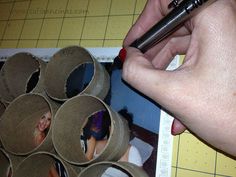 a person holding a pen near some rolled up paper rolls on a table with pictures