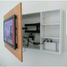 a tv mounted to the side of a white wall next to a shelf with wires