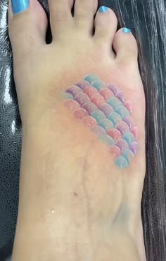 a person has a tattoo on their foot that is shaped like a rainbow fish scale