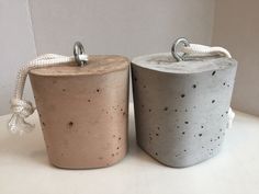 two cement containers with rope handles on top of a white table next to each other