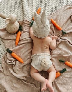 a baby laying on top of a bed next to carrots and a stuffed animal