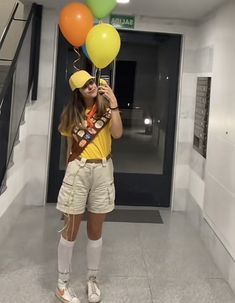 a woman in yellow shirt and shorts holding balloons