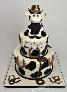 a birthday cake decorated with a cow and horseshoes on the bottom tier is shown