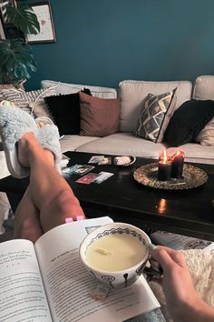 a person sitting on a couch reading a book while holding a cup of coffee in their hand