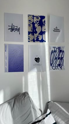 four posters on the wall above a bed in a room with white walls and pillows