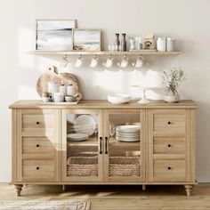 a wooden cabinet with dishes and cups on it in a white room next to a rug