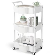 a white shelf with books, plants and other items on it's wheels for storage