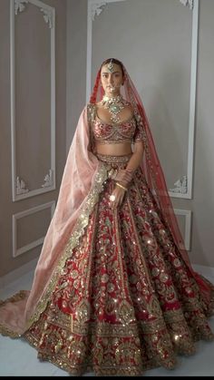 a woman in a red and gold bridal gown standing next to a white wall