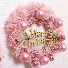 a pink wreath with merry christmas written on it and ornaments hanging from the wall behind it