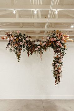 an arrangement of flowers hanging from the ceiling over a white wall in a room with exposed ceilings