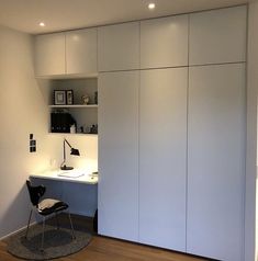 a room with a desk, chair and white cupboards on the wall next to it