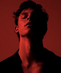 a young man with his eyes closed in the dark, looking up at something red