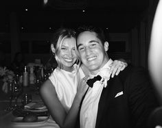 a man and woman posing for a photo at a dinner table with wine glasses in the background