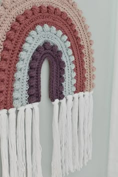 a crocheted rainbow hanging on the wall with tassels and fringes