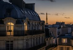 the eiffel tower is lit up in the distance behind some buildings at sunset