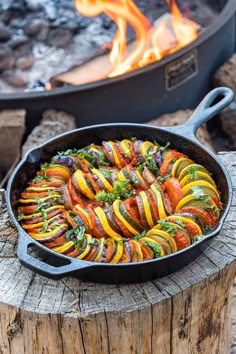 an iron skillet filled with vegetables sitting next to a fire