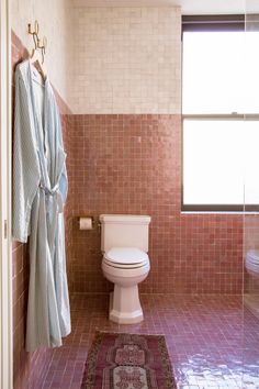 a white toilet sitting in a bathroom next to a bathrobe and rug on the floor