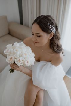 a woman sitting on a couch holding a bouquet of white flowers in her right hand