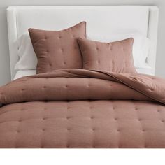 a bed with two pillows on top of it and a white headboard in the background