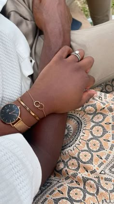 two people holding hands while sitting on a patterned table cloth with gold rings and bracelets